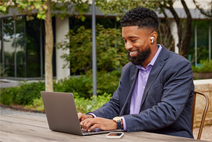 A person in business casual clothing works at a laptop while smiling. 