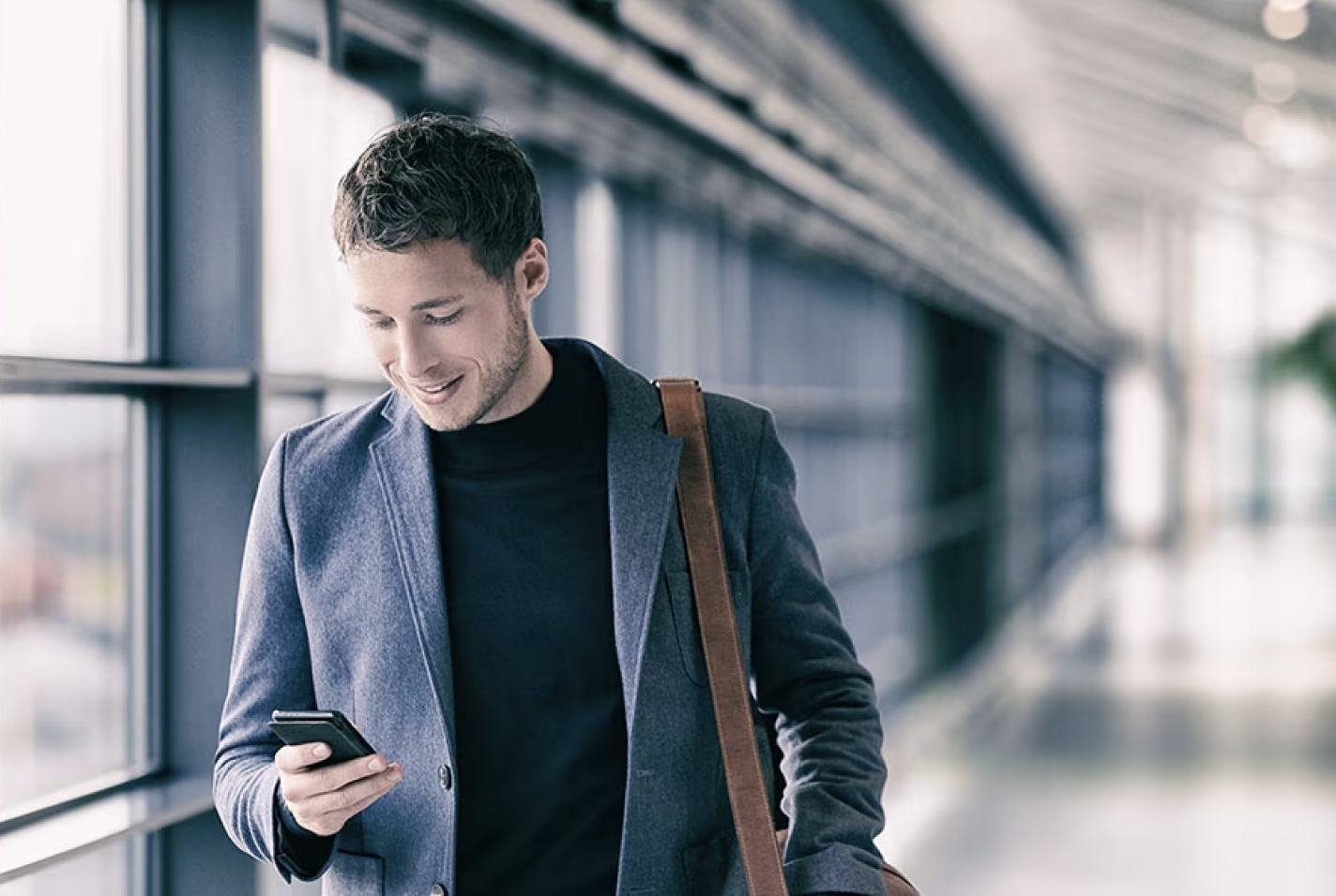 An investor walks down a hallway while looking at a smartphone.