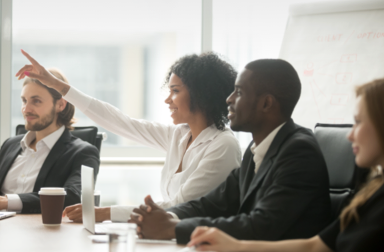 A person sitting at a conference table raises their hand.