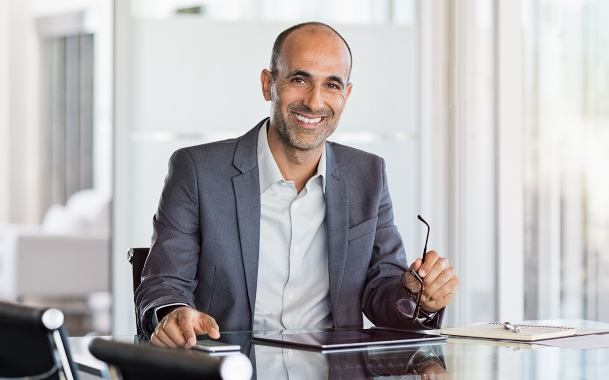 A person sitting at a desk in an office smiles and looks directly at the camera.