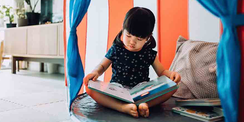 A young child, sitting on the floor and reading a book