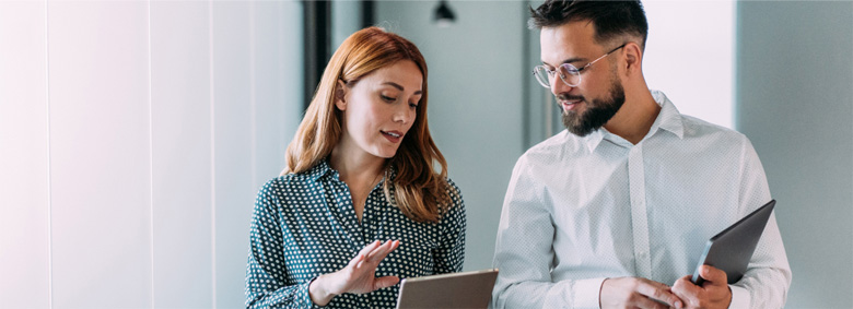 Two professionals standing and conversing while looking at a tablet.